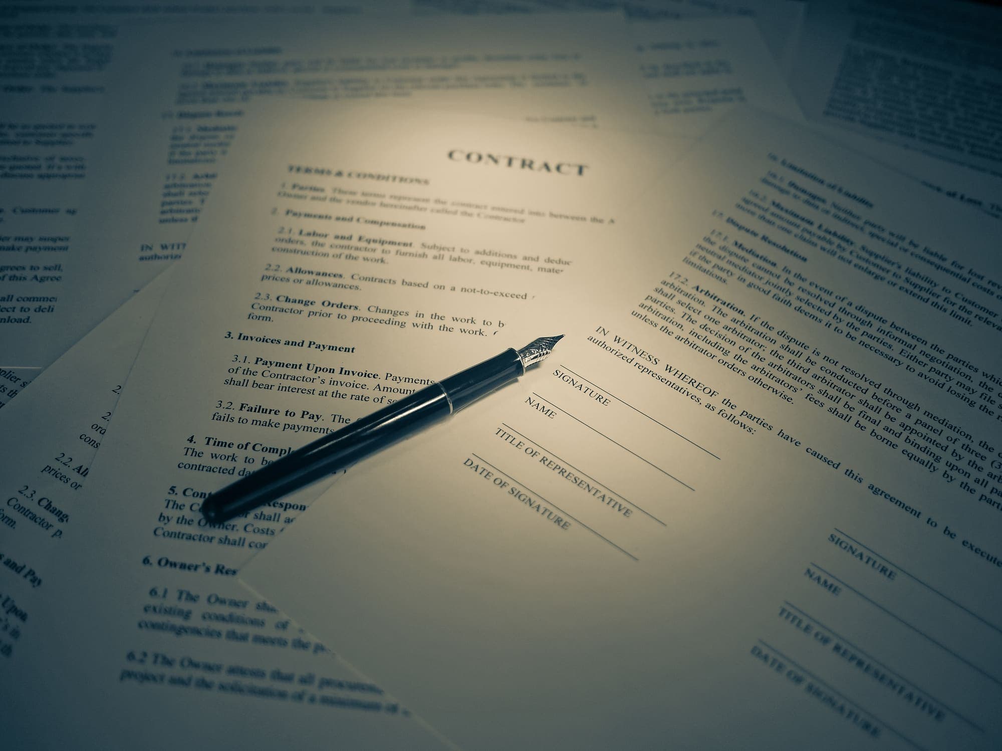 Fogli di un contratto con spazi per la firma e una penna stilografica appoggiata sopra, in luce calda
